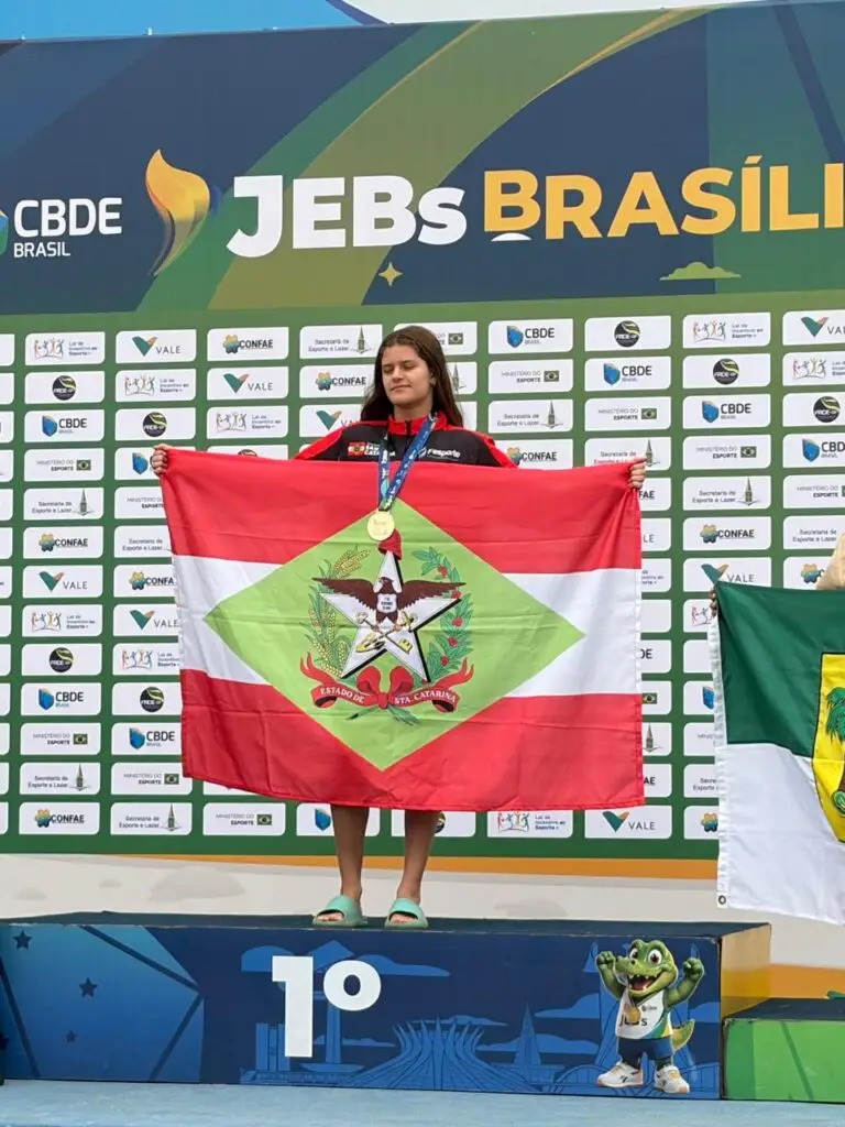 Estudante-atleta catarinense com medalha e bandeira de Santa Catarina no pódio dos JEBs Brasil